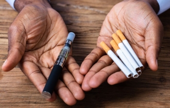 hands holding a vape pen and cigarettes