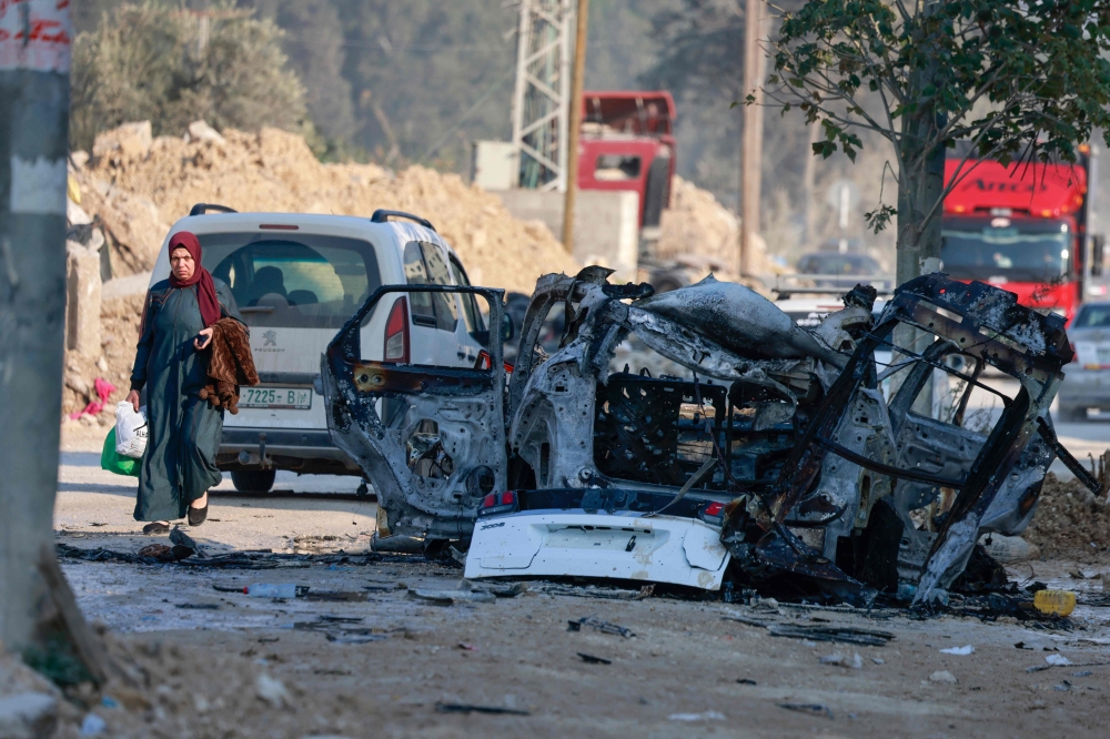 فلسطينية تمر أمام سيارة دمرت في غارة للاحتلال بالضفة الغربية- أ ف ب