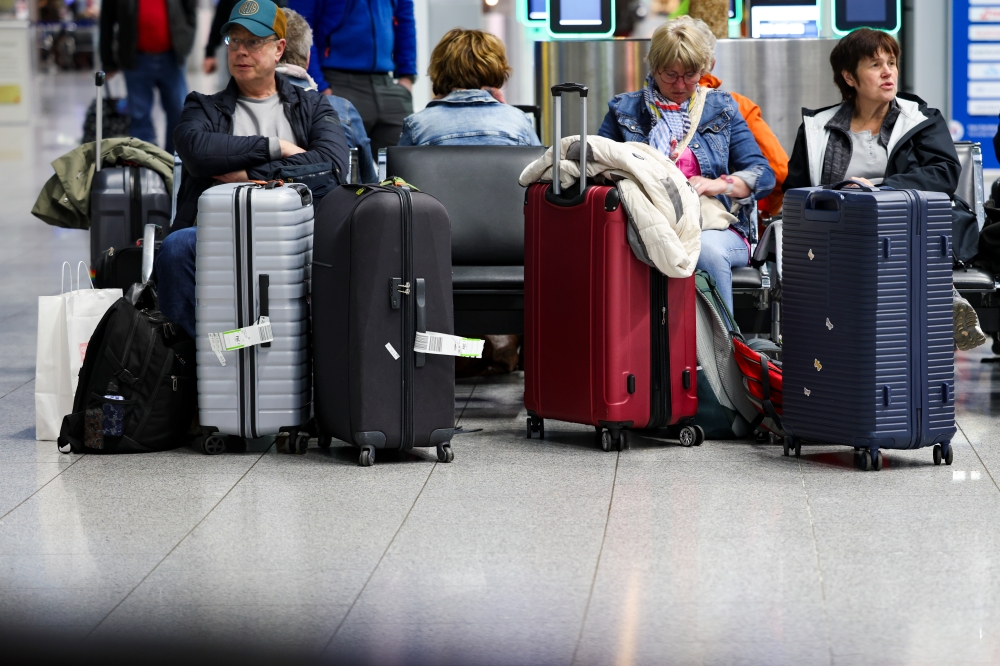 10 March 2025, North Rhine-Westphalia, Duesseldorf: Travellers wait in the departure terminal at Duesseldorf Airport beneath a display board showing a strike notice. The Verdi union has called for a 24-hour warning strike by public sector and ground handling employees at eleven airports on Monday. Photo: Christoph Reichwein/dpa