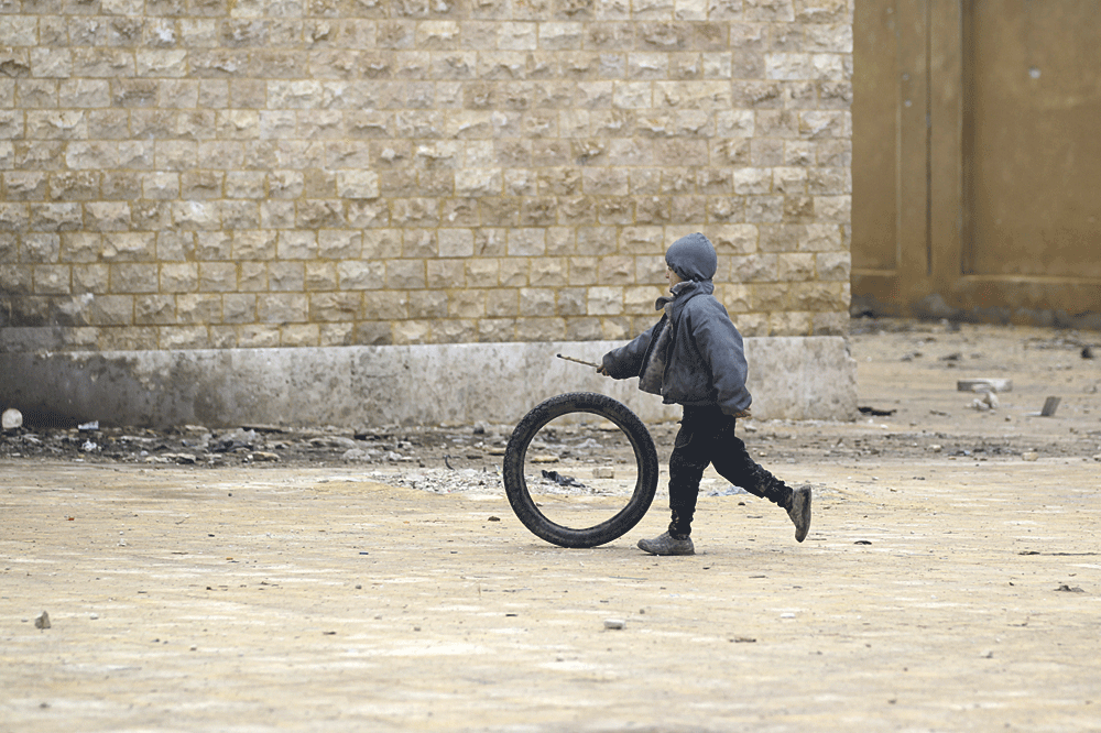 طفل يلعب بإطار سيارة أمام مدرسة دمرتها غارات الأسد شمال حلب