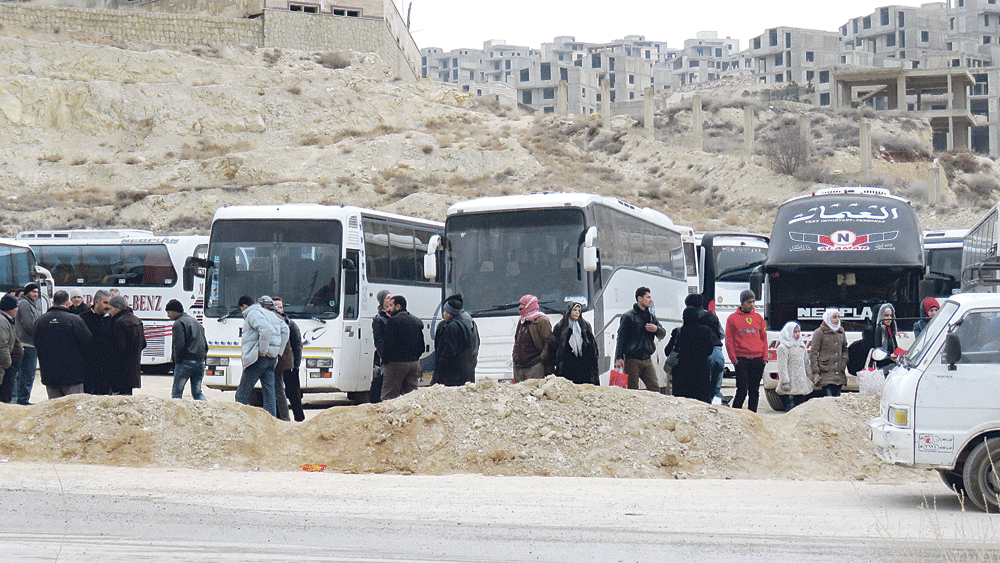 سوريون يتجمعون حول الحافلات استعدادًا لمغادرة «عين الفيجة» في وادي بردى (أ ف ب)
