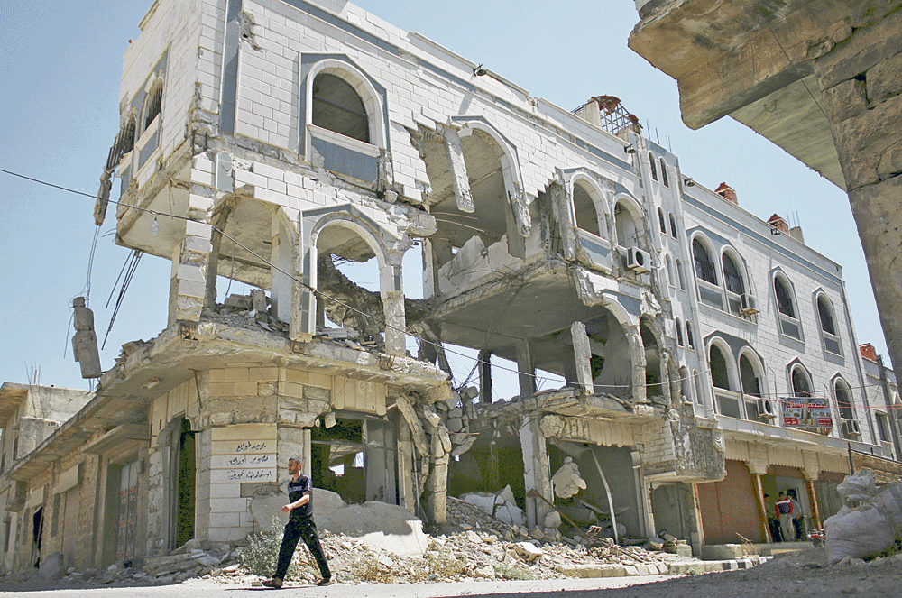 سوري يمشي أمام مبنى دمّره طيران الأسد بمدينة إنخل في درعا (رويترز)